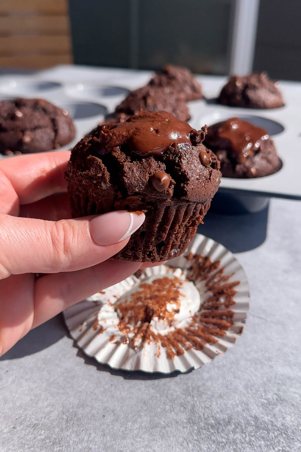 A hand holding a double chocolate muffin with ganache